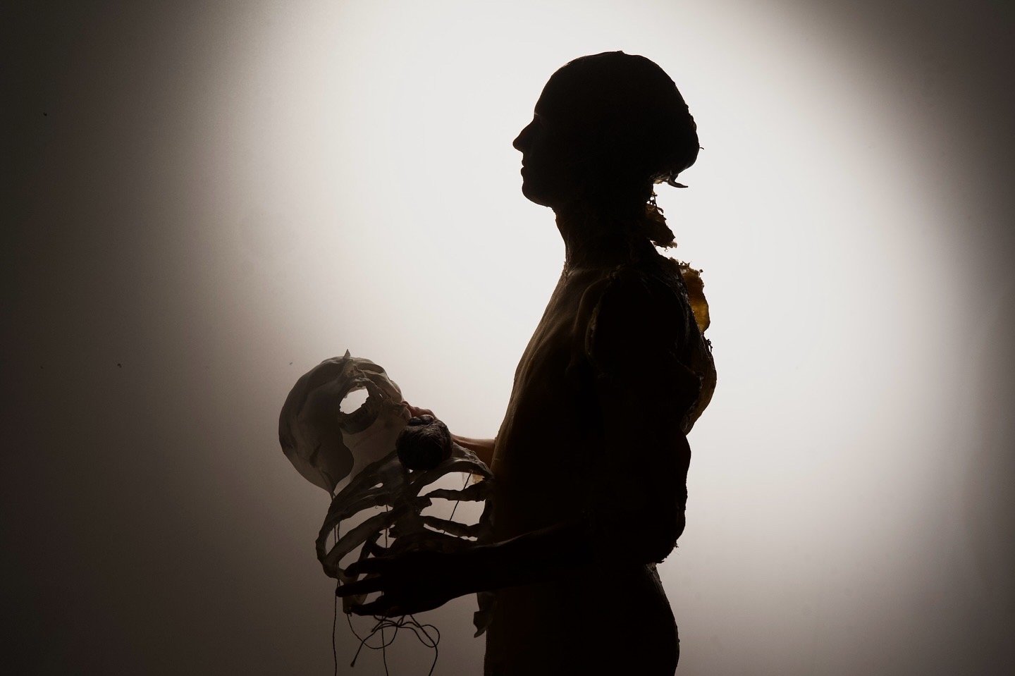 Silhouette of a woman holding a small skeleton model against a light background.