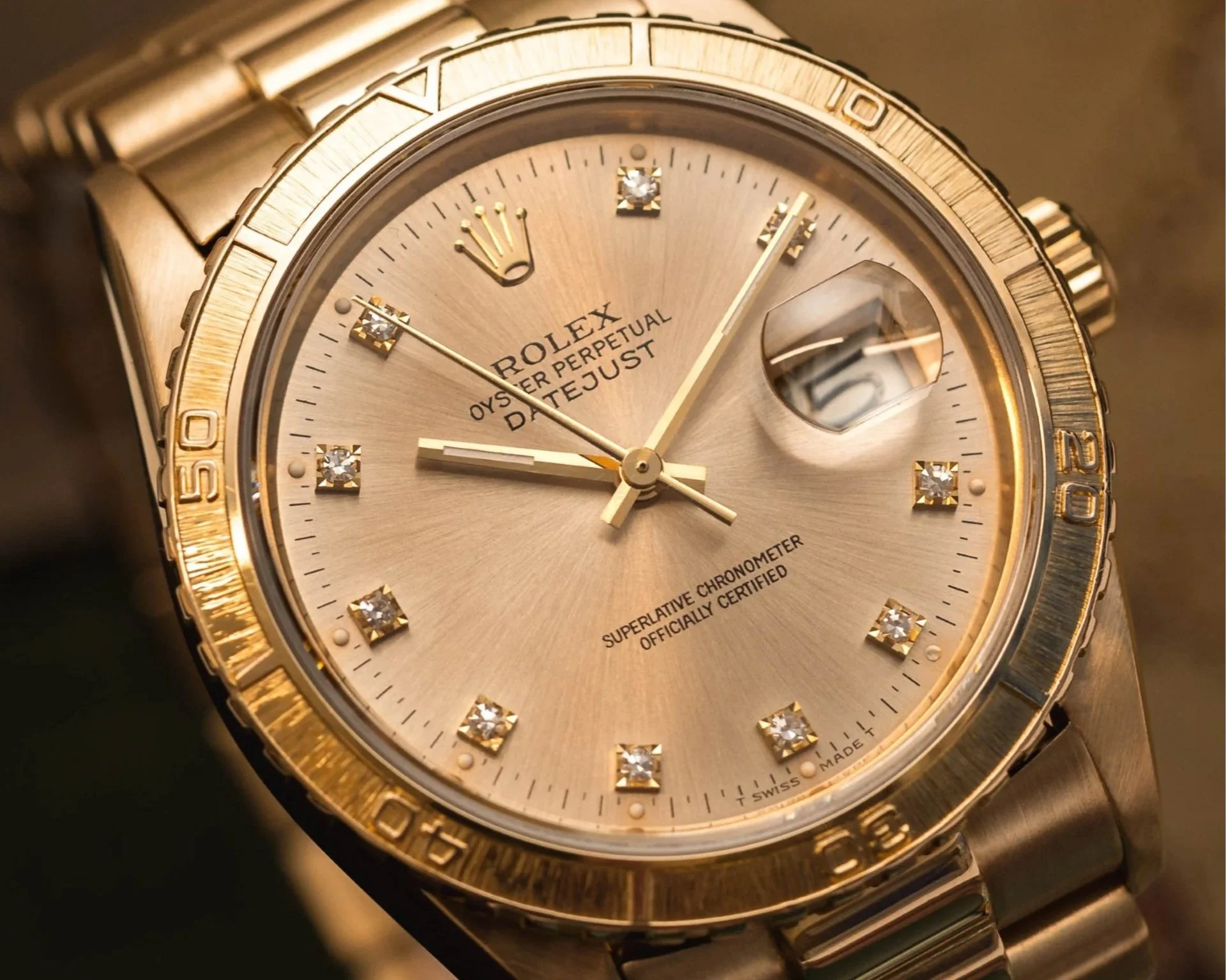 Close-up of a gold Rolex Oyster Perpetual Datejust watch with diamond hour markers and a date display magnified at 3 o'clock.