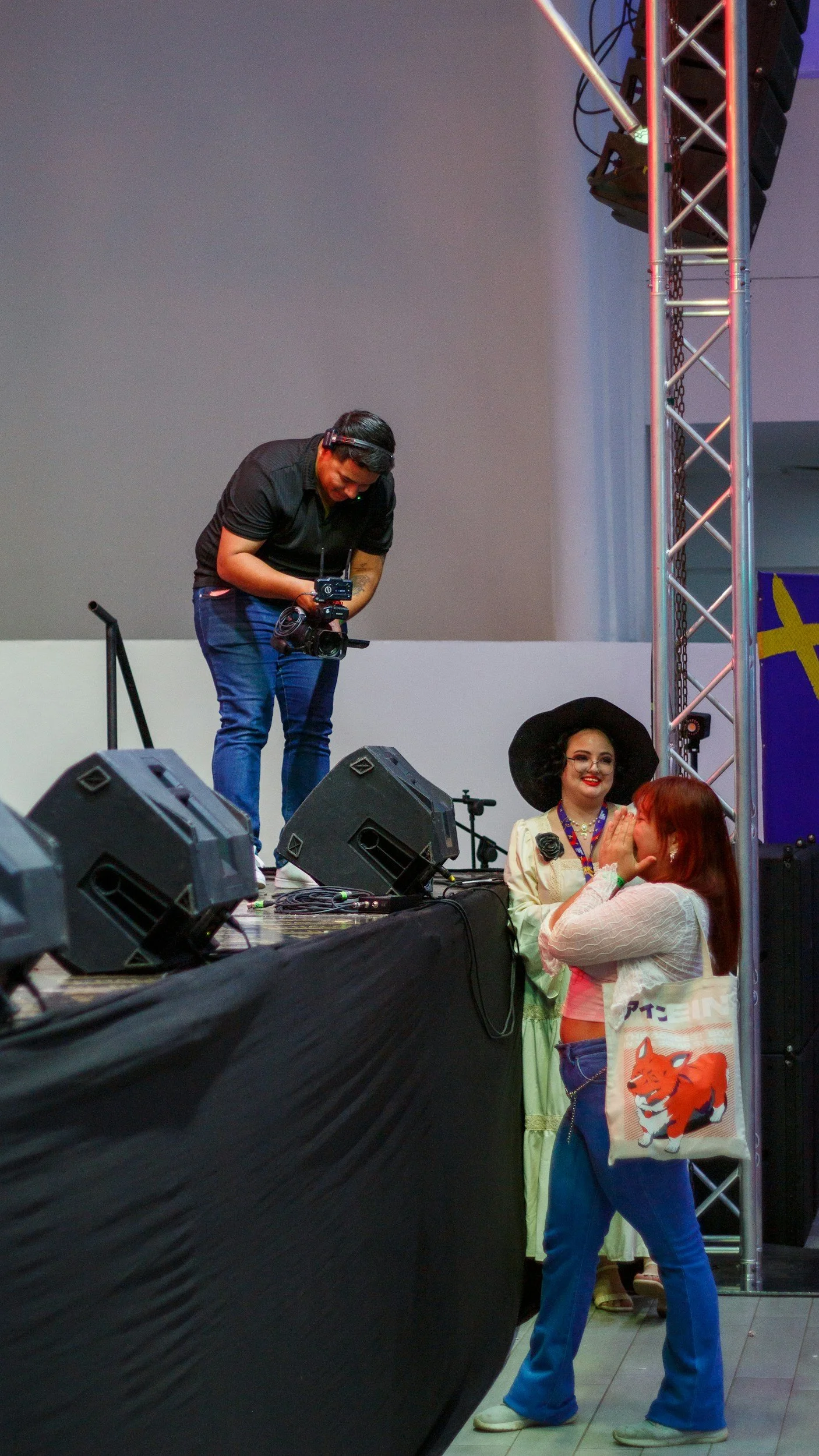 Event crew member near a stage while guests talk during an indoor event.