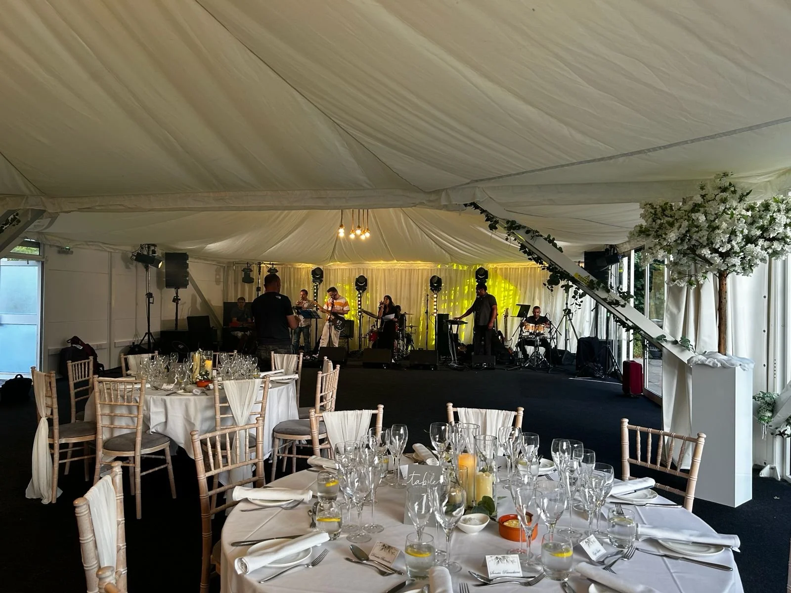 Wedding reception in an elegant marquee with decorated tables and a live band performing on stage.