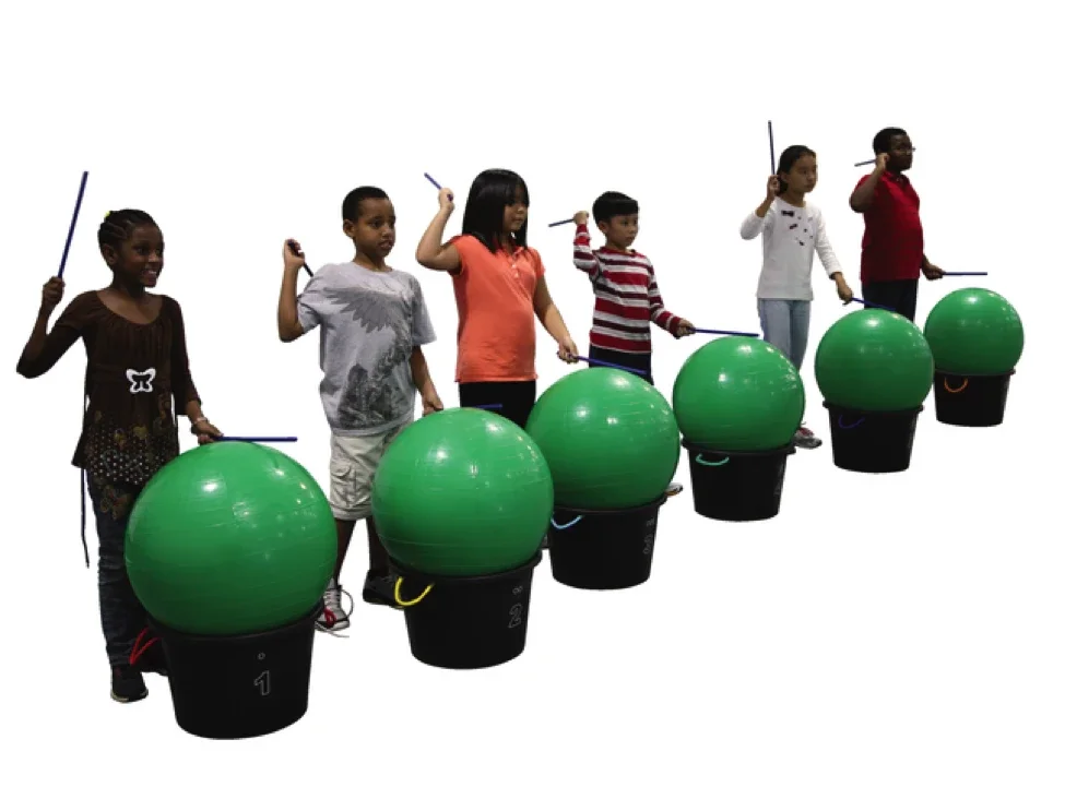 Group of kids each in front of a large green ball holding drum sticks to make noise against the ball