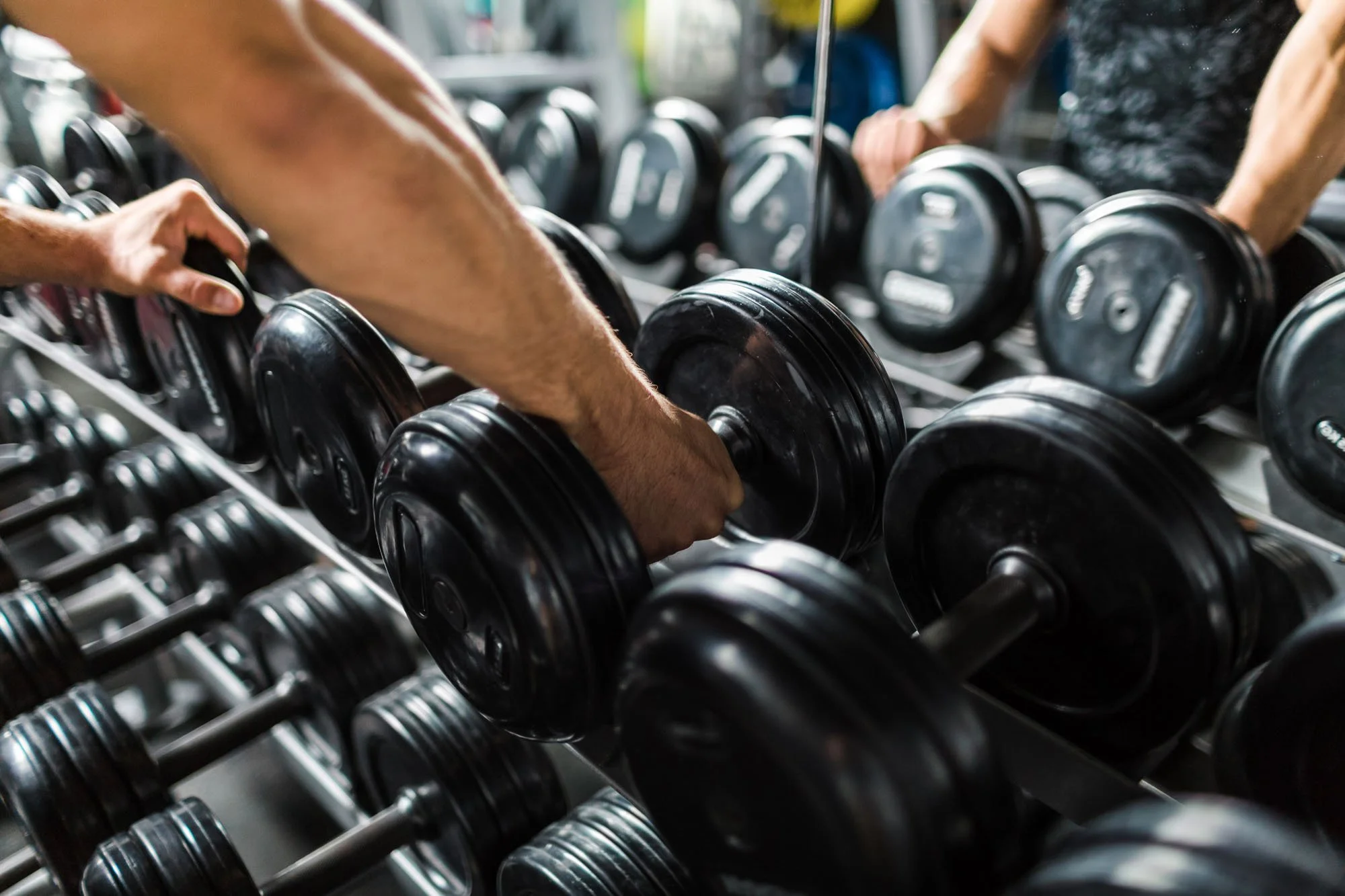A person adjusting black dumbbells on a rack in a gym.