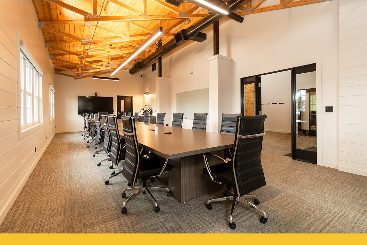 Large meeting room with large table with 20+ seats, warm lighting, large TV and whiteboard