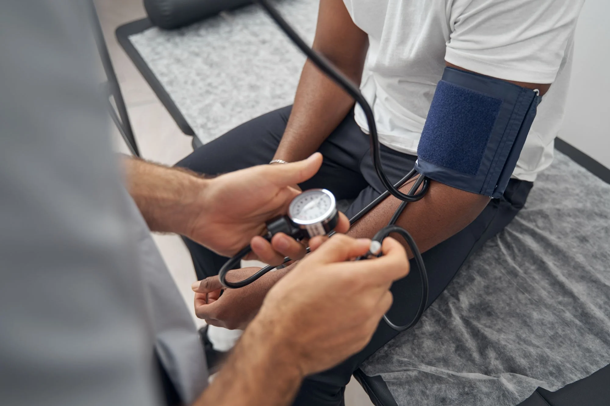 A healthcare worker measures a patient's blood pressure using a sphygmomanometer, with the patient seated in a chair.