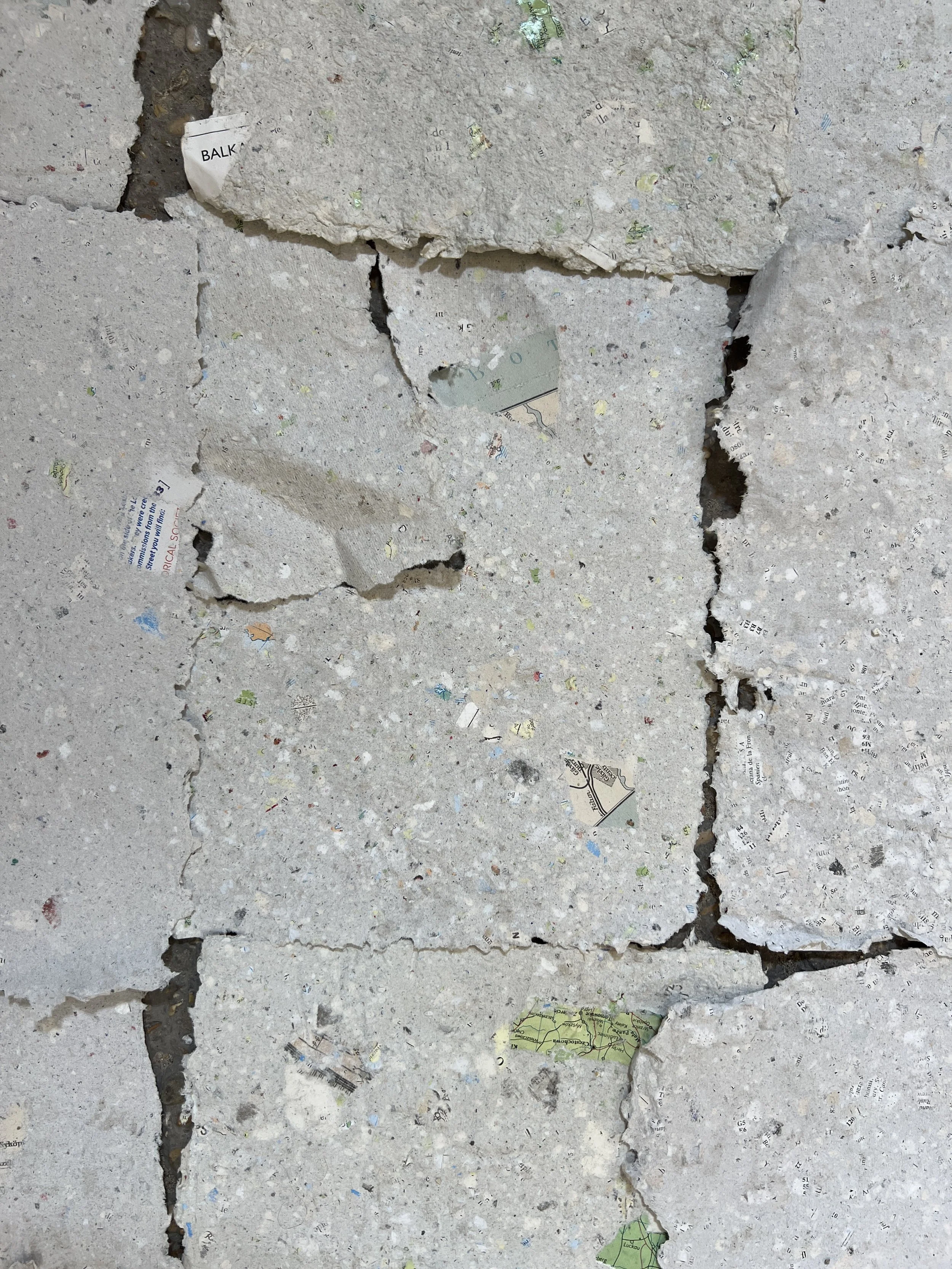 Broken concrete floor with embedded torn and crumpled pieces of paper and small debris.