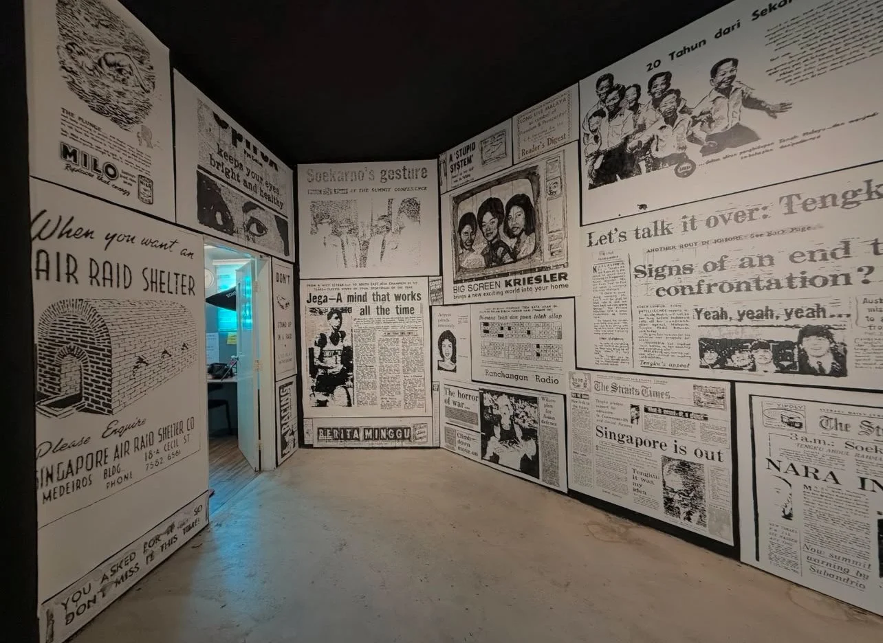 Room with walls covered in black and white newspaper-style posters and articles, including illustrations, headlines, and photographs. There is a doorway with a blueish light coming through.