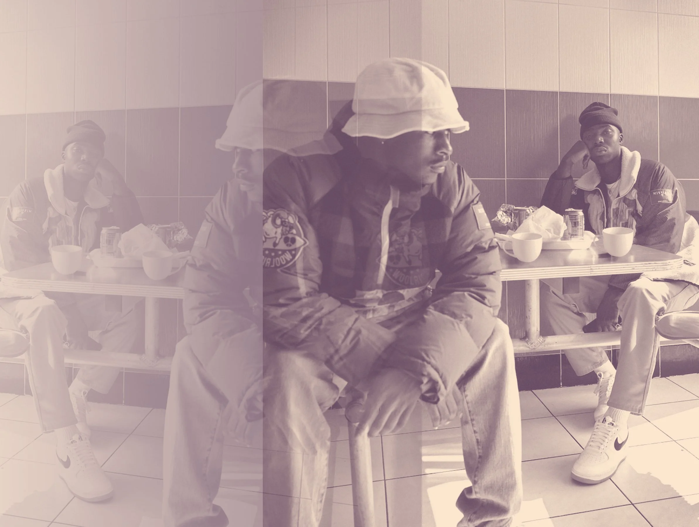 Three young men sitting at a table in a cafeteria, wearing casual clothing, with cups and cans of soda in front of them.