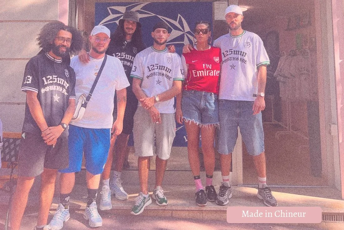Group of seven young adults standing together outside a store, wearing casual summer clothes, some with sports jerseys, shorts, and sneakers.