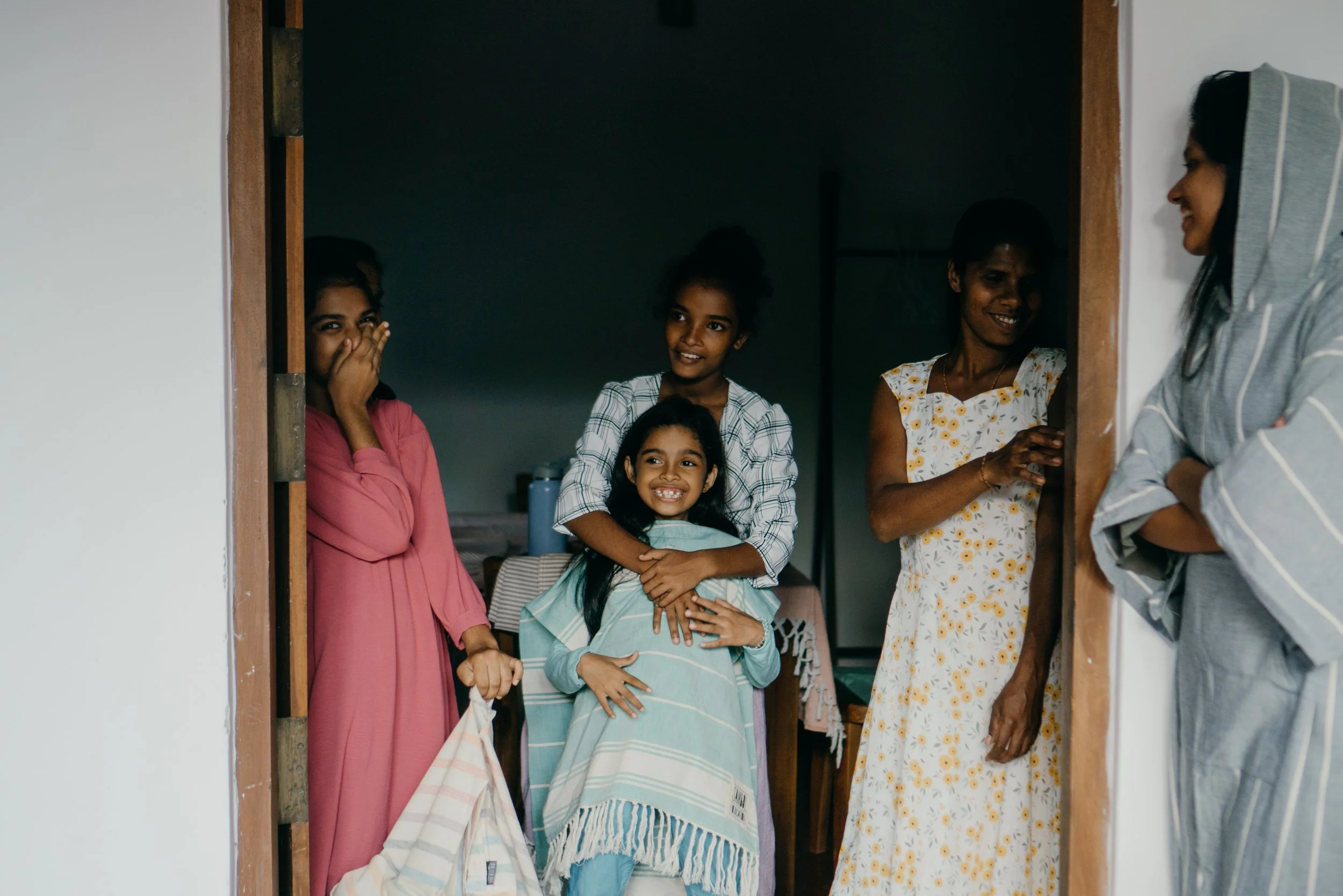 Fünf Frauen und vier Kinder, die in einem Haus lachen und Spaß haben, einige sind in der Türöffnung, andere im Raum. Es sieht aus, als ob sie sich unterhalten.