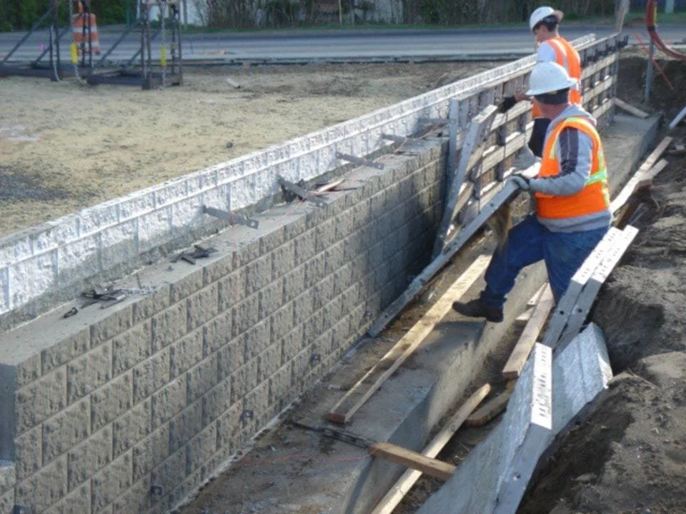 Construction workers building a brick retaining wall on a construction site, wearing safety vests and helmets.