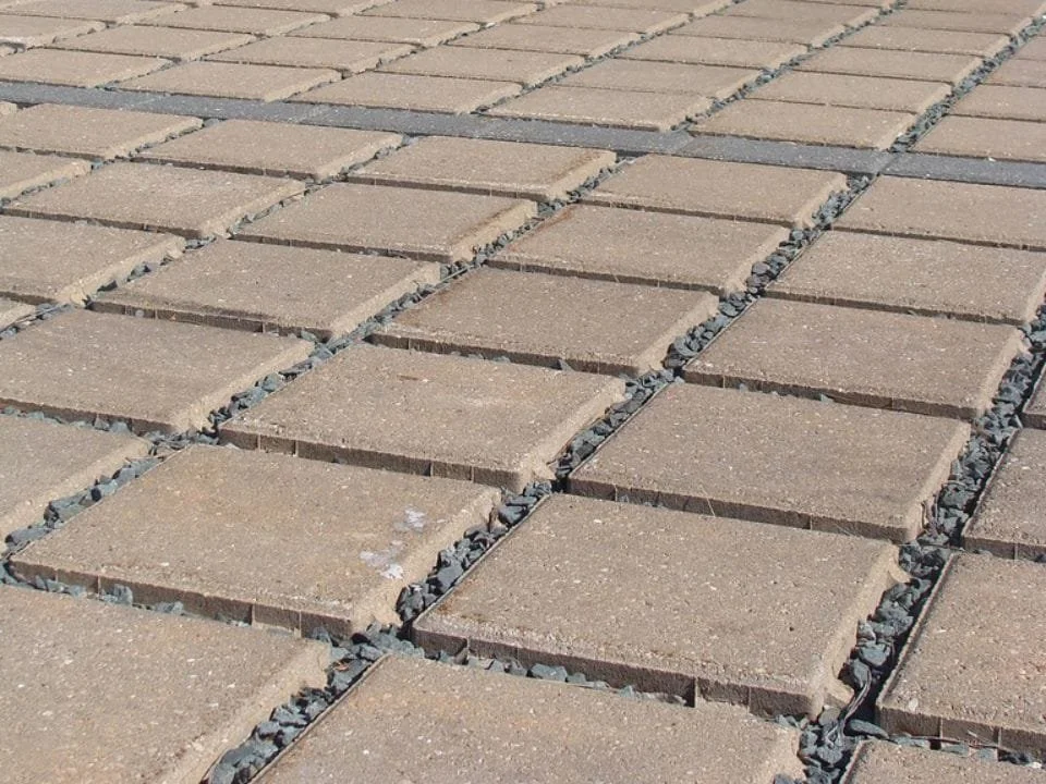 Close-up of a paved walkway made of beige square concrete tiles with dark gray gravel in the gaps between them.