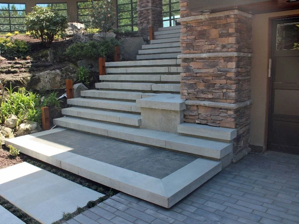 Stone steps leading up to a porch with a brick and stone exterior wall, surrounded by landscaped plants and rocks.
