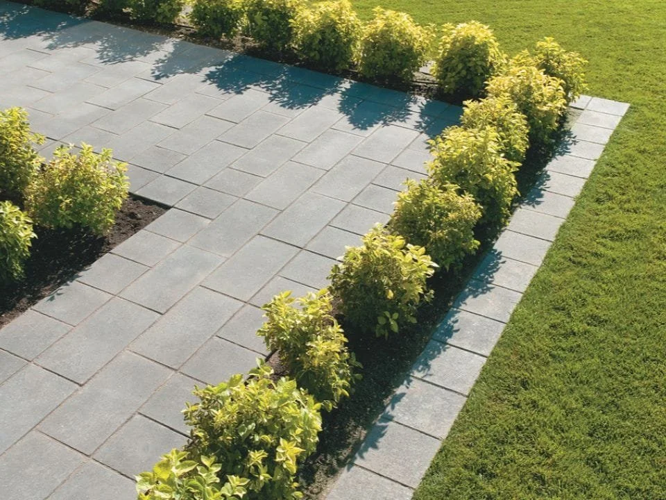 A neatly landscaped garden area with gray paving stones and green bushes, bordered by a strip of grass.