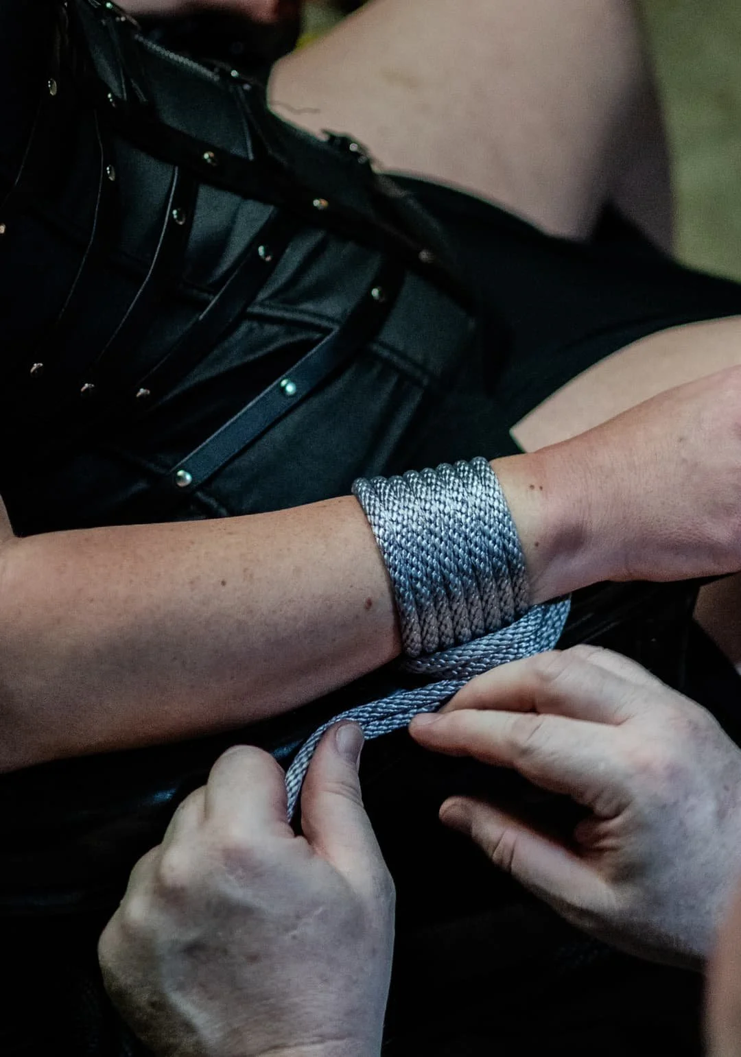 A person with their hands tied with a silver rope, while another person is tying the knot.
