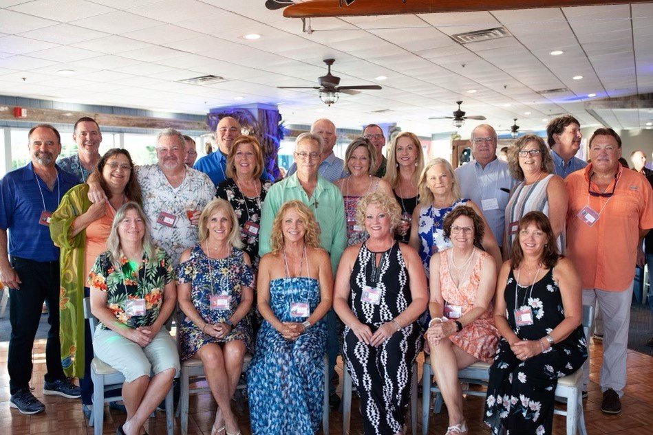 A group of people gathered in a room, posing for a group photo at an event or conference. The group includes men and women, some sitting and others standing, all smiling.