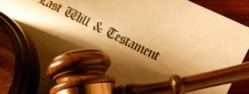 Close-up of a wooden gavel, a mirror, and a document titled 'Last Will & Testament' on a wooden surface.