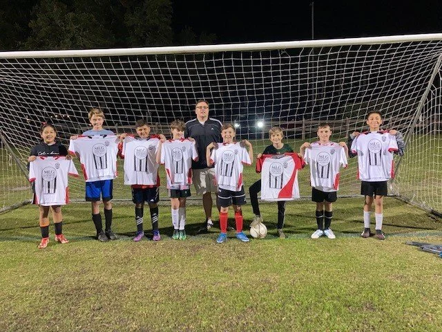 Youth soccer team with their coach holding jerseys on a soccer field at night.