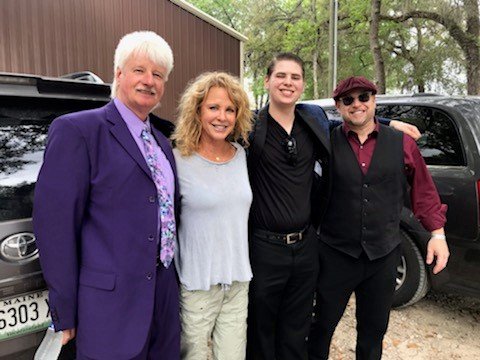 Four people standing outdoors near parked cars, smiling at the camera.