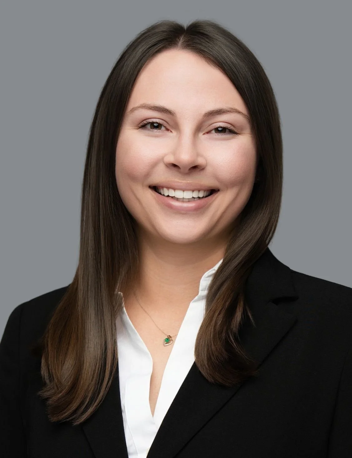 Professional woman with brown hair smiling in a black blazer and white shirt, against a gray background.