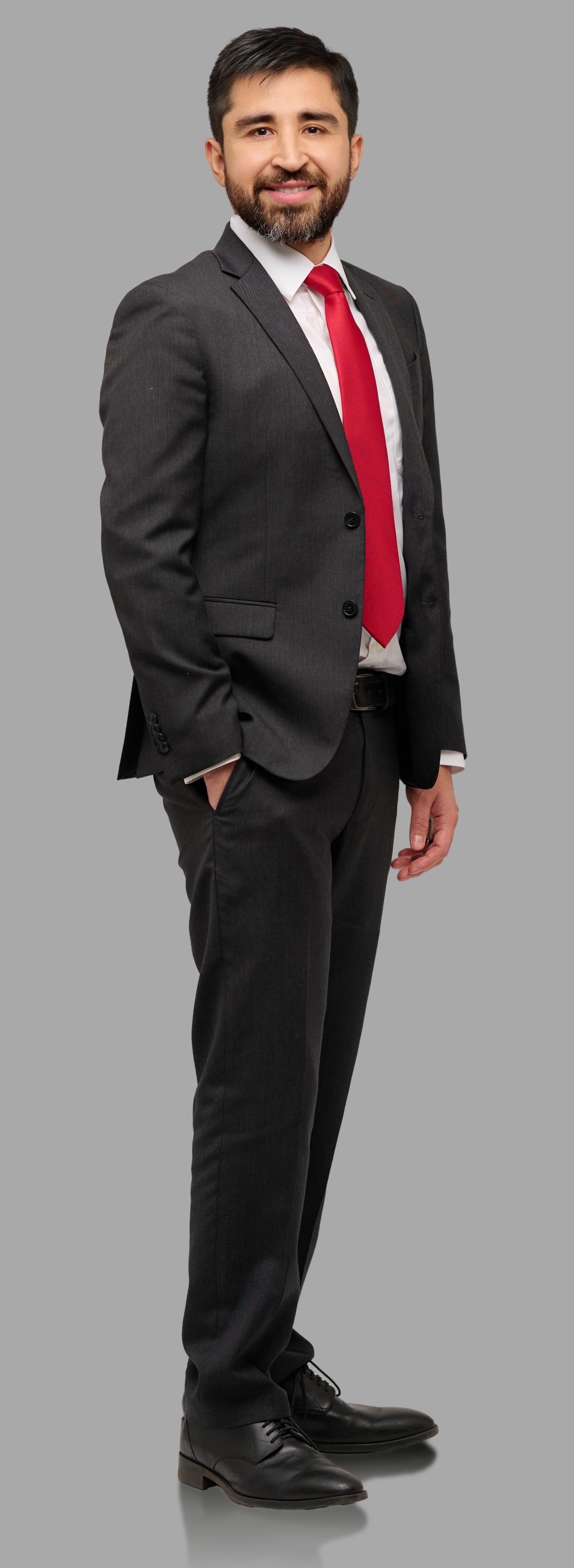A man in a gray suit, white shirt, and red tie smiling, standing against a plain gray background.