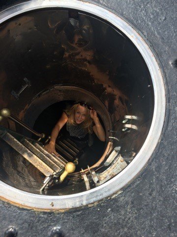 A woman looks up through a manhole opening, with her hand on the ladder, as she climbs out of the manhole.