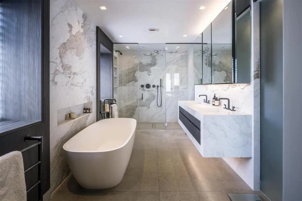 Modern bathroom with a freestanding bathtub, glass shower with a rainfall showerhead, marble countertops, and large mirror.