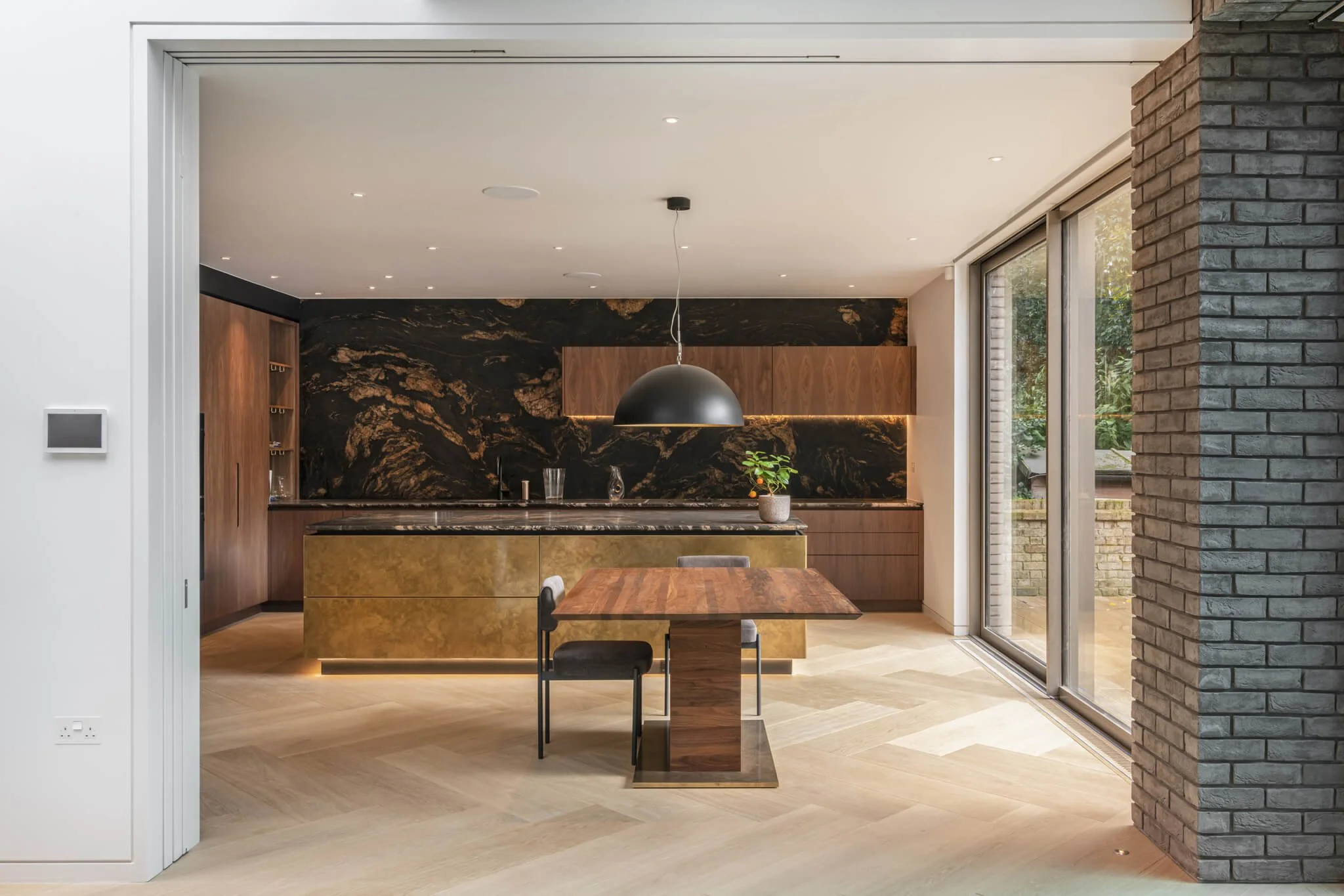 Modern open-concept kitchen with dark marble backsplash, wooden cabinetry, a black dome pendant light, and large sliding glass doors leading outside.