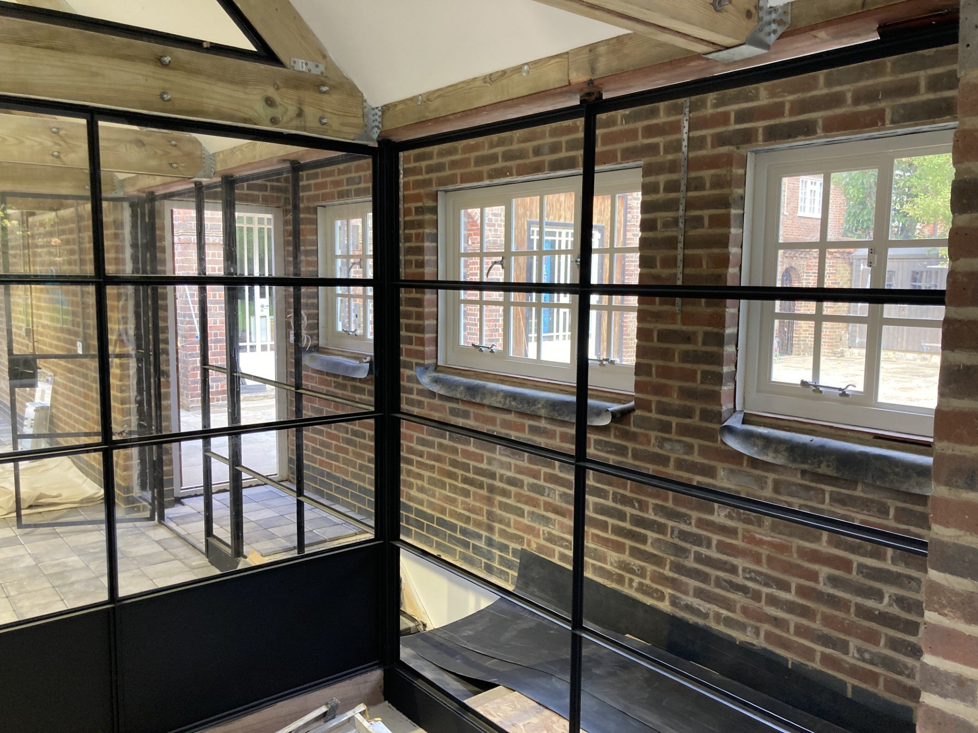 Interior of a building under construction with brick walls, three windows, and a metal and wood framing structure.
