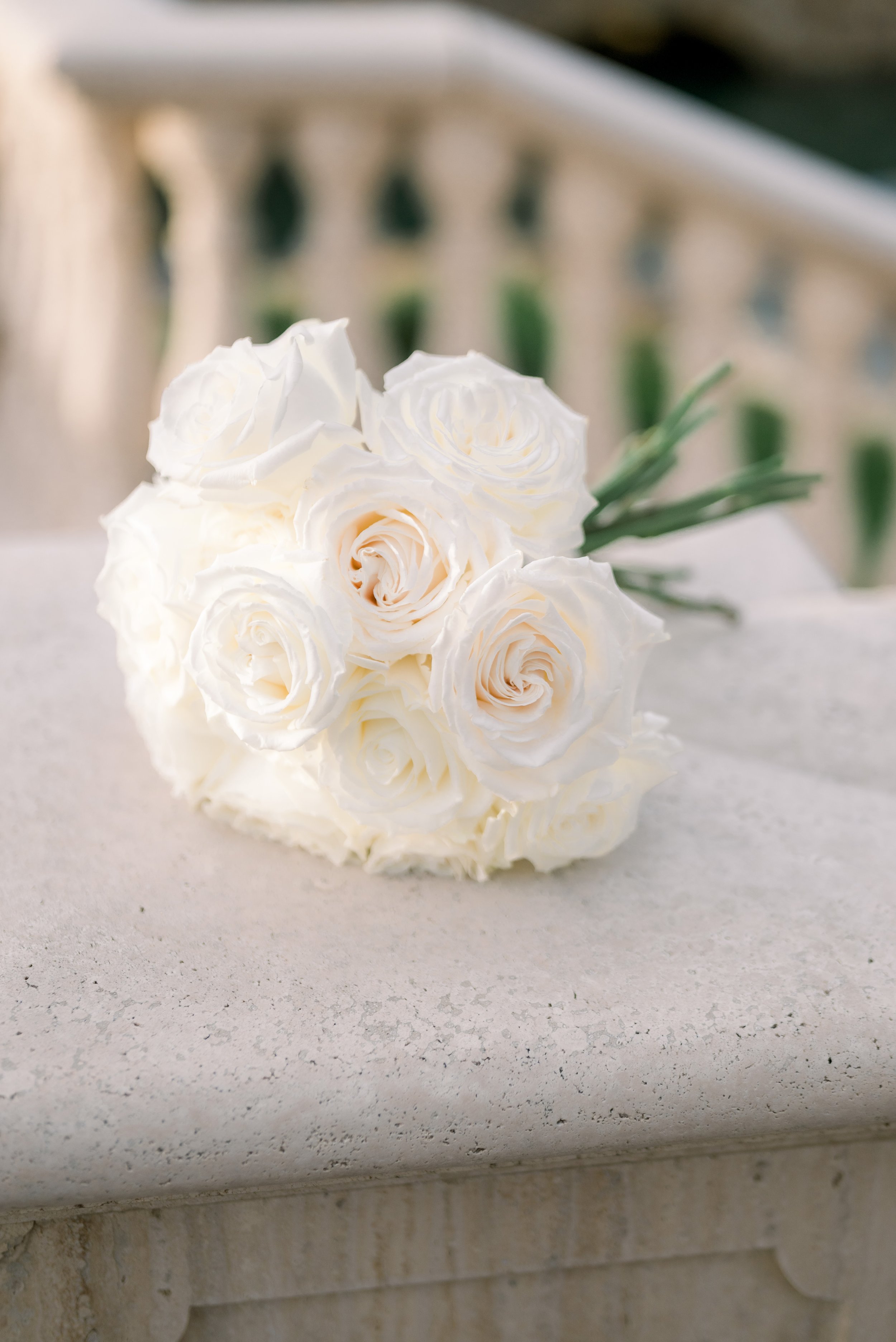 A bouquet of white roses placed on a white stone surface near a textured wall.