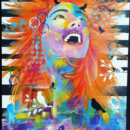 Colorful graffiti mural of a smiling woman with vibrant orange hair surrounded by black birds and abstract patterns.