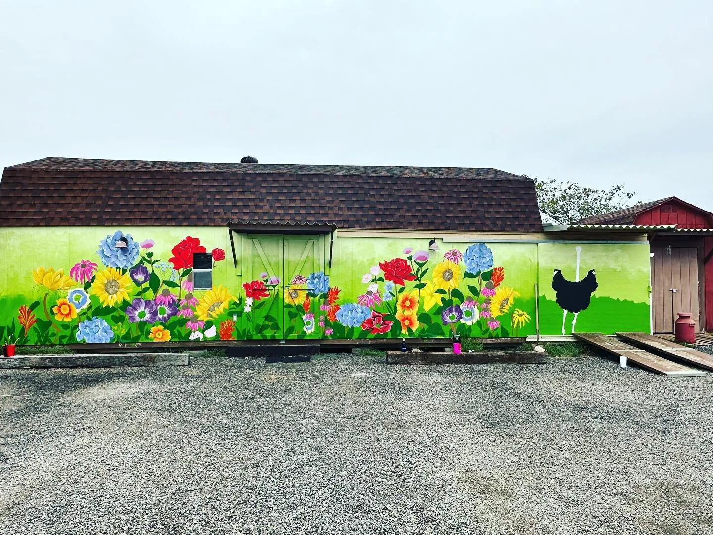 Colorful mural of various flowers, a black silhouette of a dog, and a green hill on a building wall.