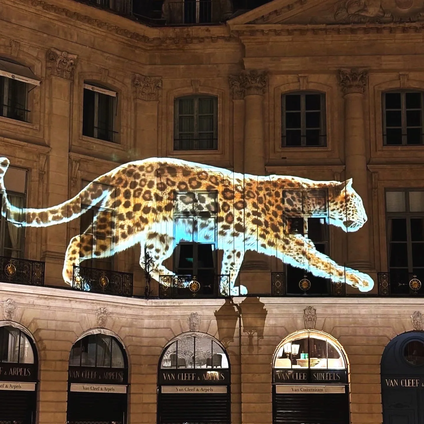 Nighttime city scene with historic building, street lamps, parked motorcycles and cars, and a full moon in the sky.