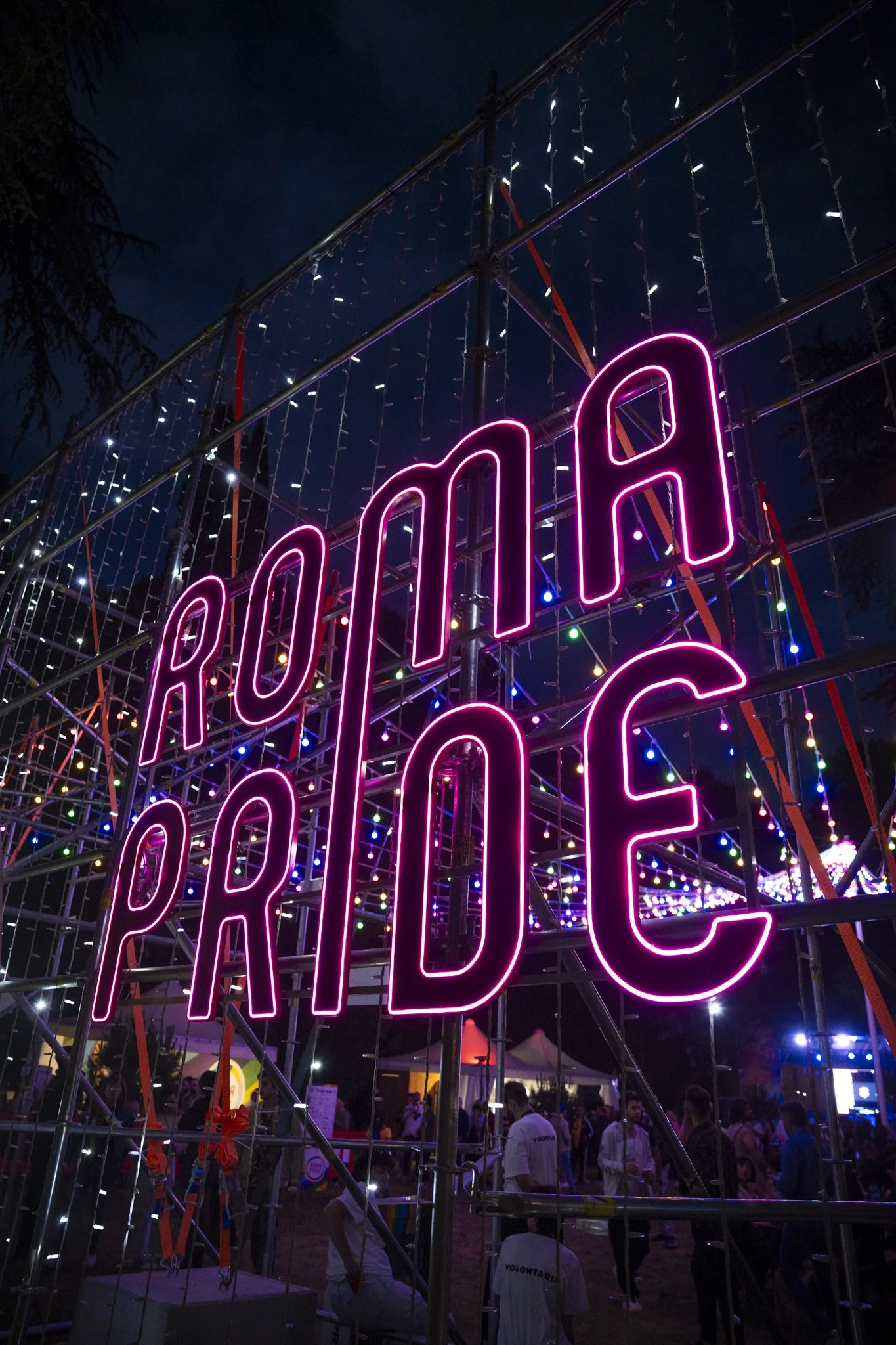 Neon sign spelling out the word 'PARADE' amid carnival lights and a crowd of festival-goers at nighttime.