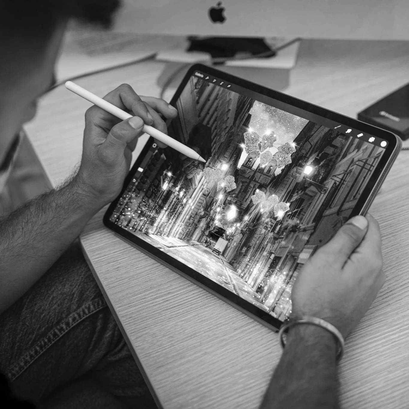 Person using a tablet with a stylus, displaying a city street scene with Christmas or holiday decorations, while sitting at a wooden table.