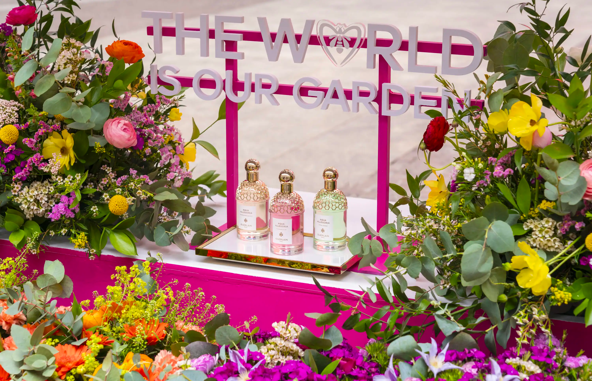 Pink display with perfume bottles from Guerlain surrounded by colorful flowers and greenery with a sign that reads "The World Is Our Garden"