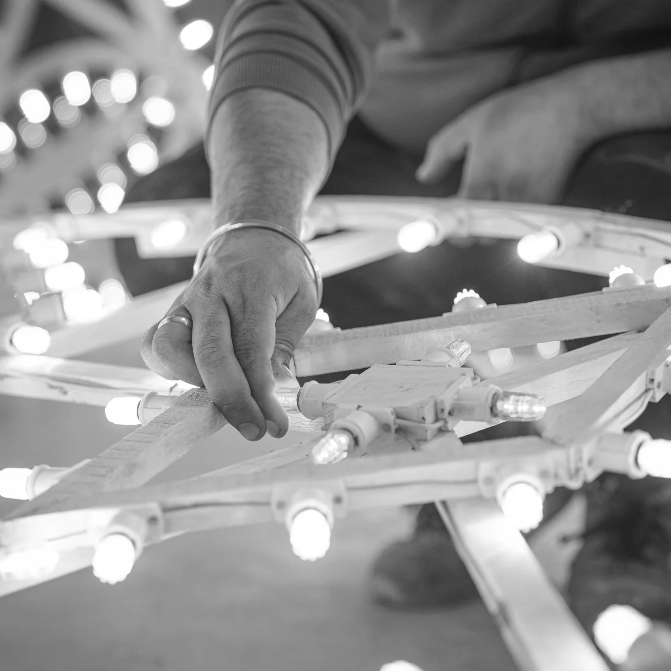 Close-up of a person's hand adjusting a decorative light fixture with light bulbs, black and white photography.