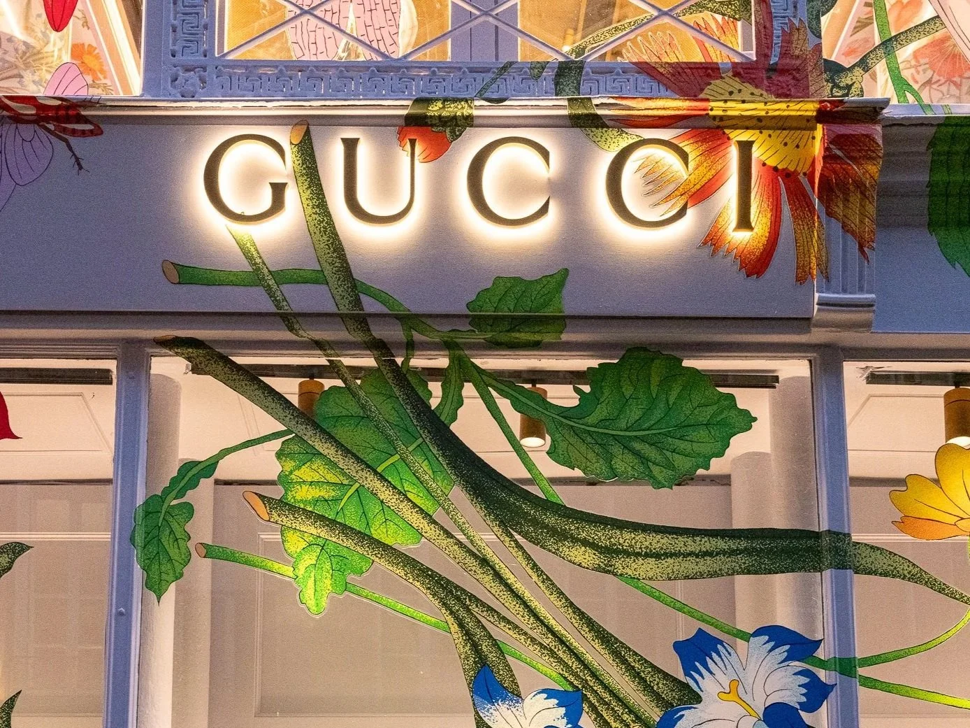 Gucci store sign with illuminated letters, surrounded by colorful floral and leaf artwork.
