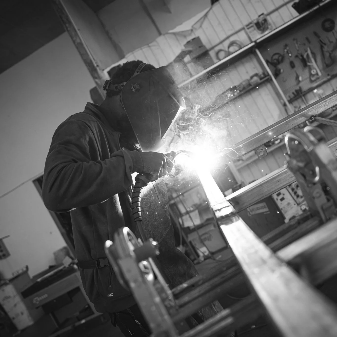 A person welding metal in a workshop, wearing protective gear including a welding helmet and gloves.