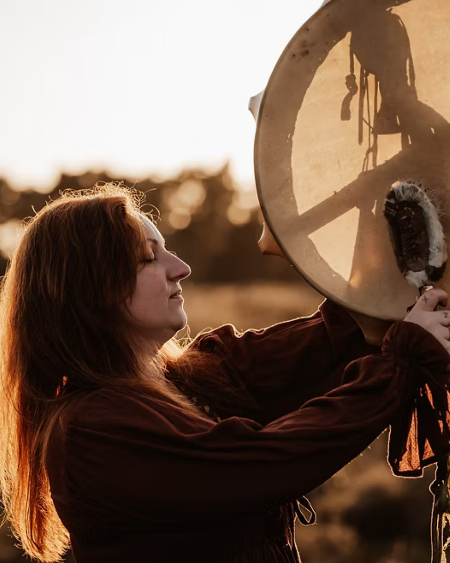 Izih Deer Kam holding a large drum outdoors during sunset.