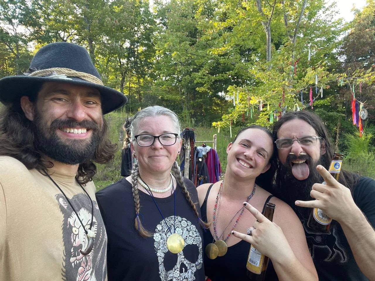 Four people smiling outdoors, two men and two women, with trees and colorful ribbons hanging in the background.