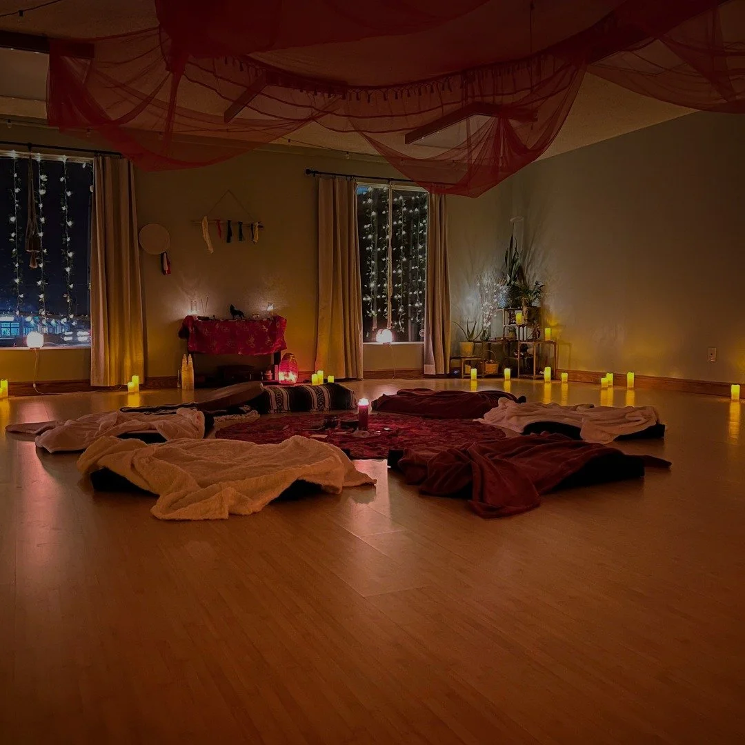 A dimly lit room decorated with string lights, candles, and draped fabrics. Sofas and blankets are arranged on the floor, suggesting a cozy or ritual setting.