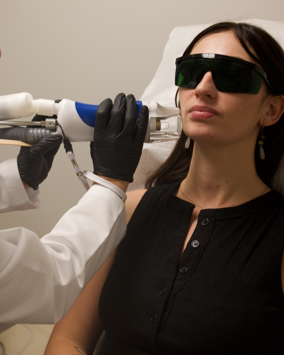 A woman undergoing a medical procedure with a specialized device, wearing protective black glasses, in a clinical setting.