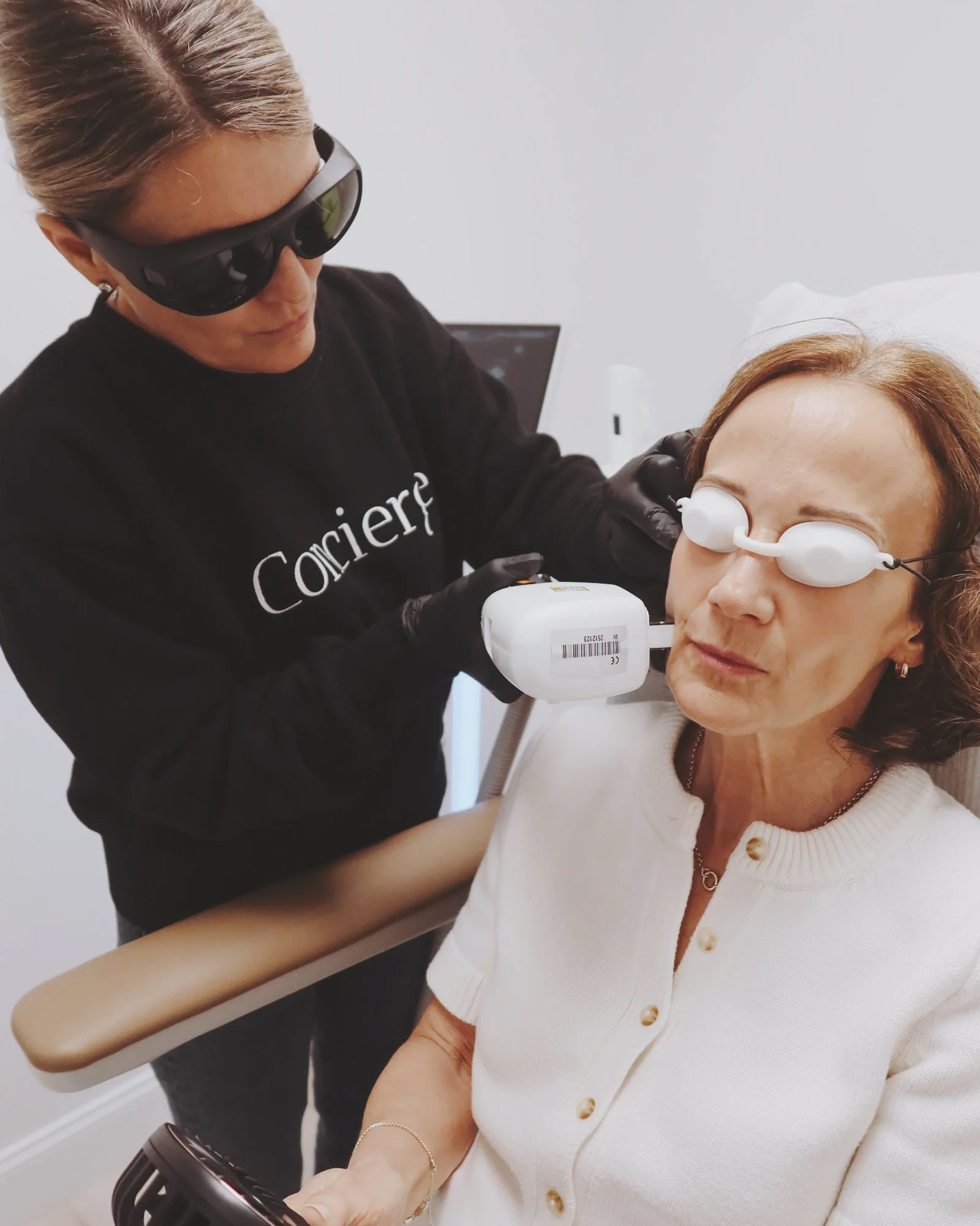 A woman receiving a cosmetic or dermatological laser treatment on her arm by a professional wearing protective glasses and gloves.