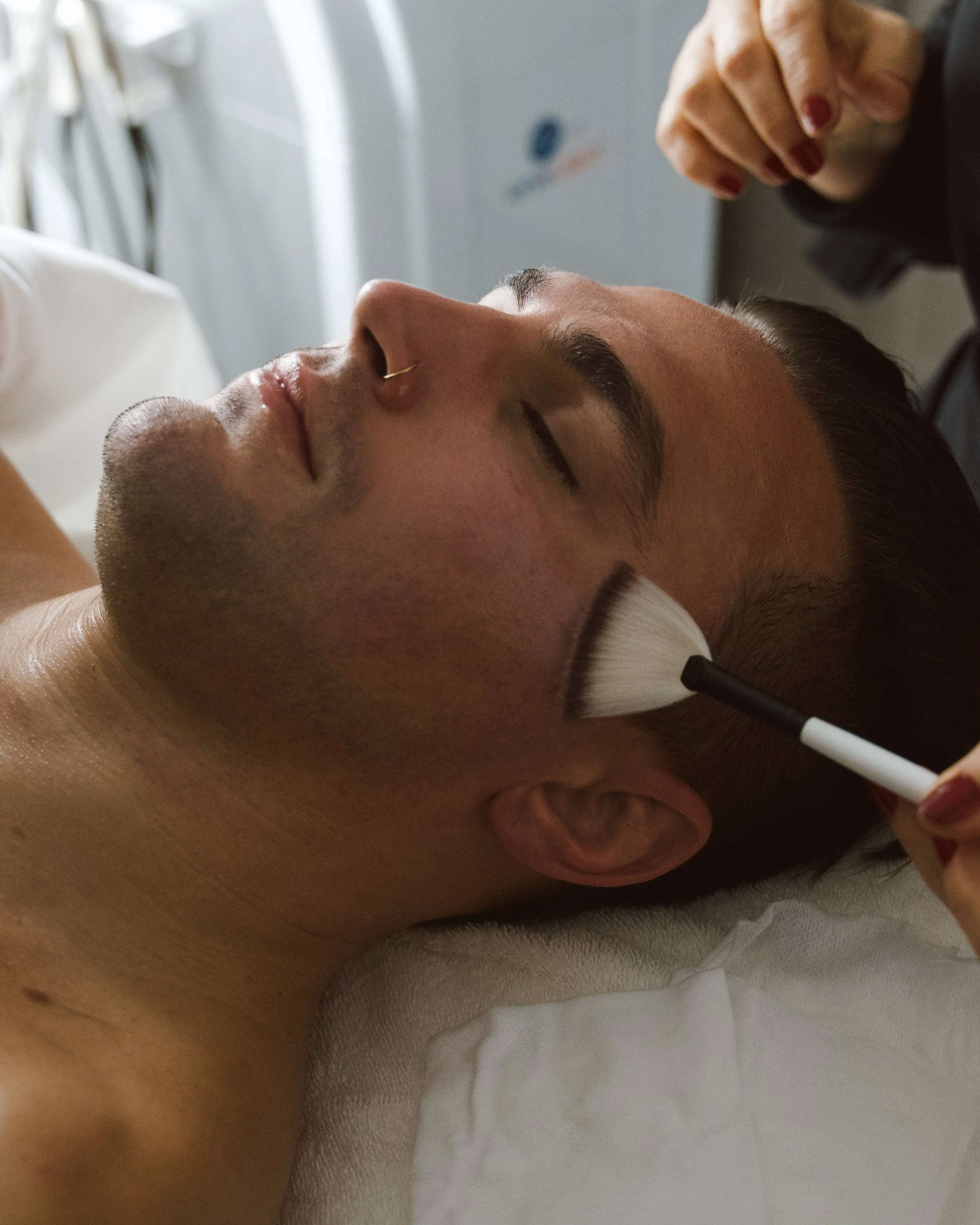 A person lying down with their eyes closed, receiving a facial or massage, with a professional's hand nearby.