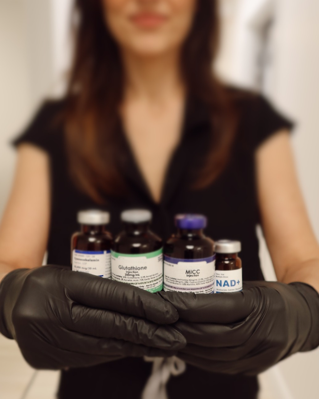 A woman wearing black gloves holding multiple small medication bottles labeled with medical ingredients.