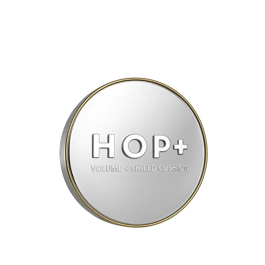 A compact container labeled 'HOP+' with the description 'Volume + Shield Cushion' underneath, featuring a sleek metallic silver design with a gold rim.