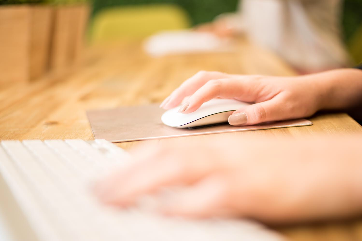 Close-up of a person's hand using a computer mouse on a wooden desk.