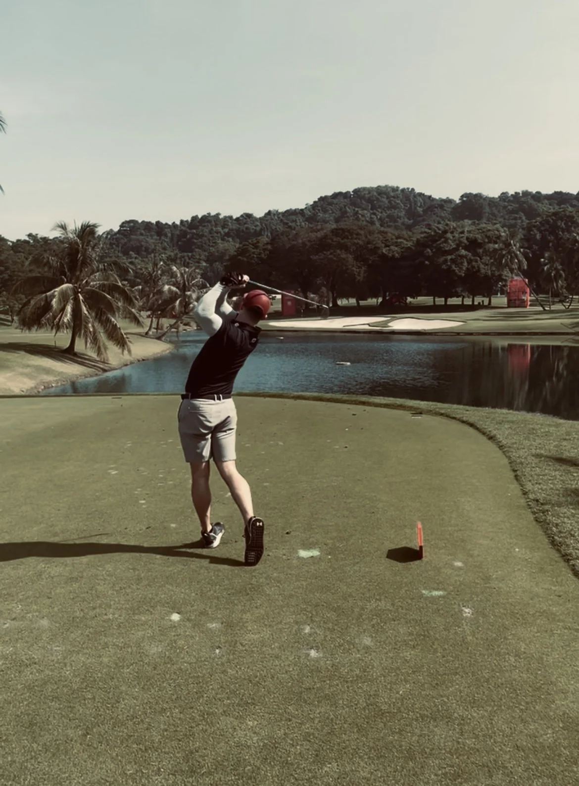 A person playing golf on a course near a pond with trees and hills in the background.