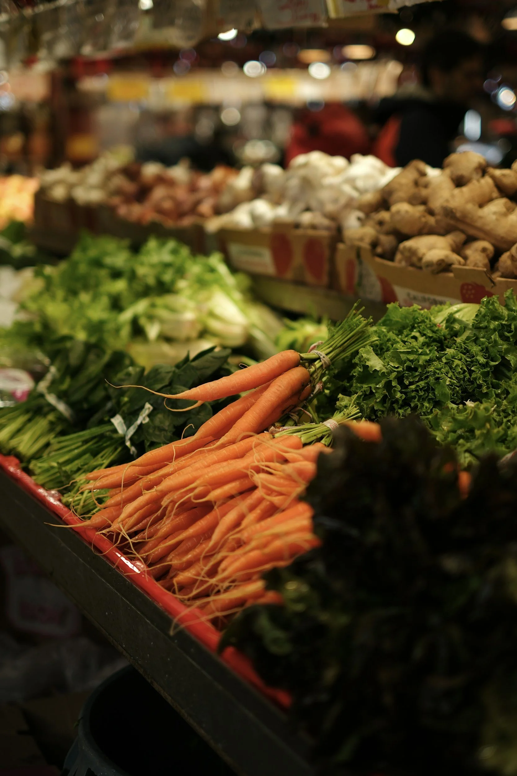 Légumes frais au marché, notamment des carottes, du chou frisé, du céleri et du gingembre, avec d'autres légumes en arrière-plan.