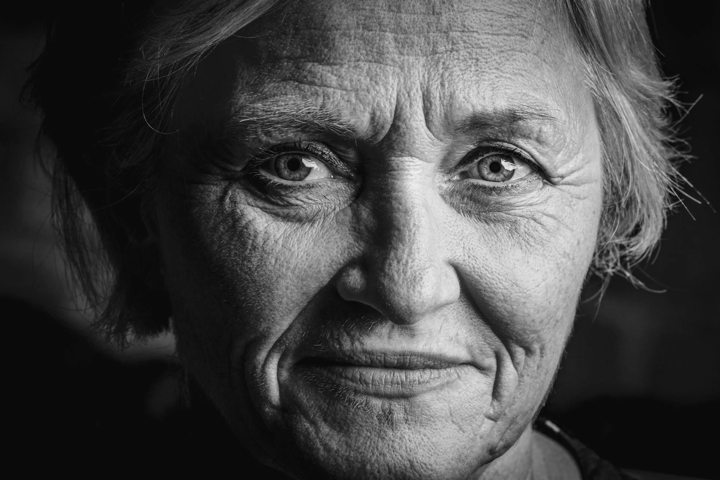 Portrait en noir et blanc d'une personne âgée avec expression intense, montrant une expression faciale forte et une peau riche en détails.
